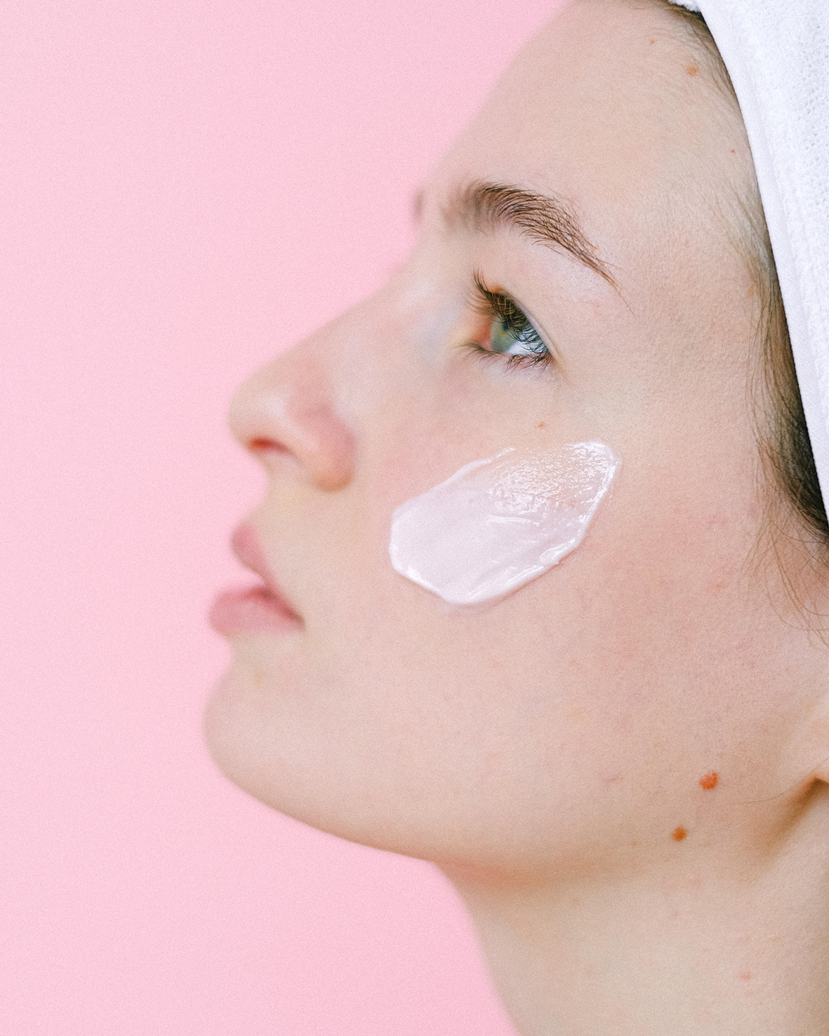 A woman uses a cleansing facial milk made from natural raw materials. The woman is standing in front of a pink background.